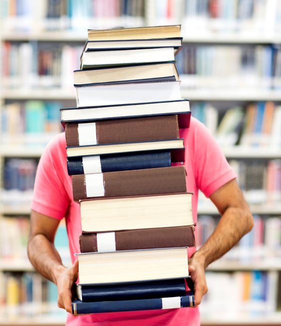 Male student carrying heavy books at the library