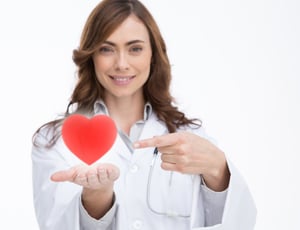 Pretty doctor holding and pointing at a red heart